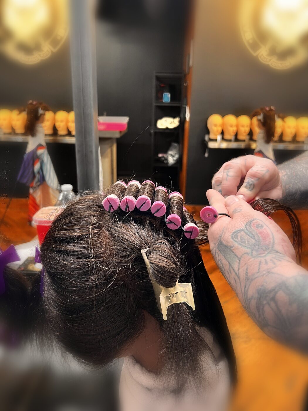 Pink perm rods set on a training head, mannequin shelf behind